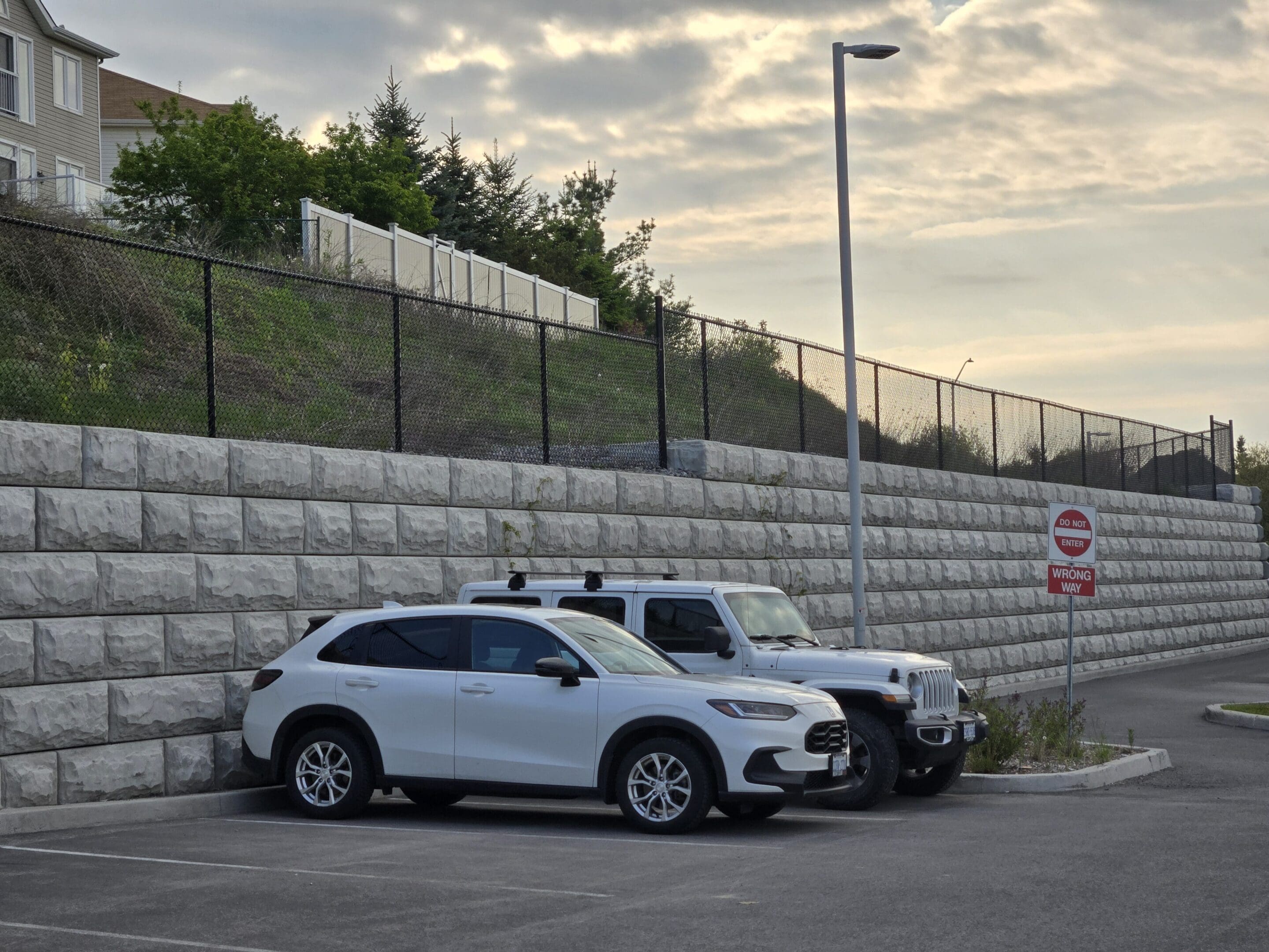 Two white cars parked in a parking lot next to a stone wall.