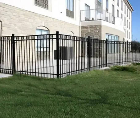 A fence that is in the grass near some buildings.